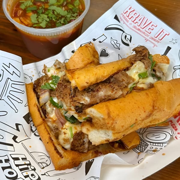 A Krave It cheesesteak sandwich with melted cheese and a side of dipping sauce.