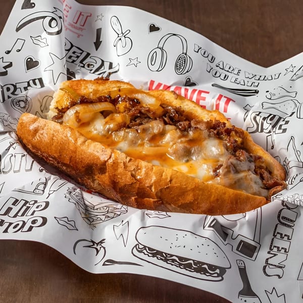 Cheesesteak sandwich with melted cheese and caramelized onions on a toasted hero, in Krave It branded paper.
