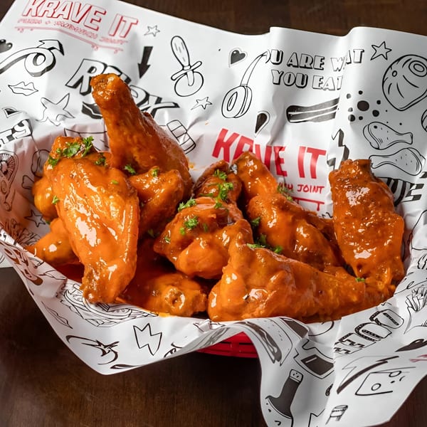 Krave It's buffalo wings, coated in orange sauce and parsley, served in a branded paper-lined basket.