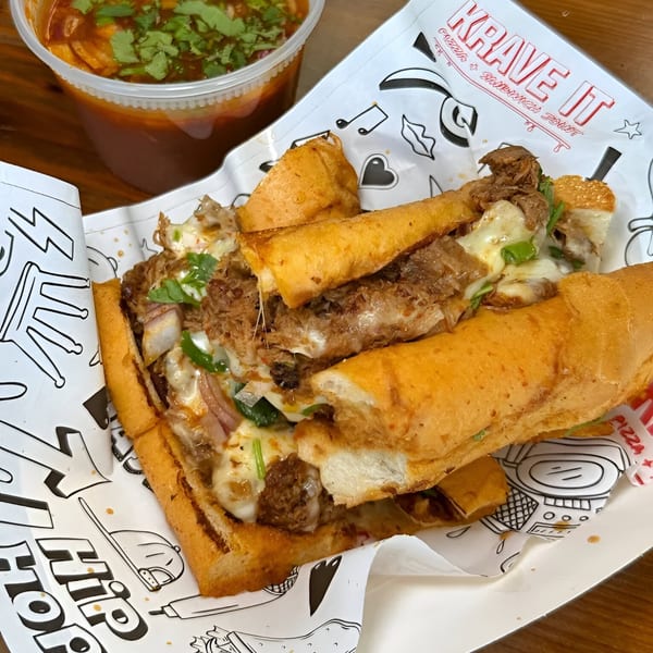 A Krave It sandwich with melted cheese and meat, alongside a cup of dipping sauce.