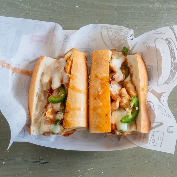 Two halves of a Krave It chicken sandwich with melted cheese and green peppers on branded paper.