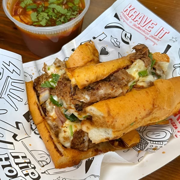 Krave It's cheesy steak sandwich with onions and cilantro, alongside a cup of dipping sauce.