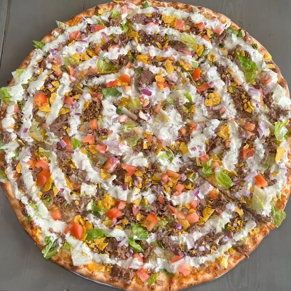 A Krave It pizza topped with ground beef, lettuce, tomatoes, red onions, and a white sauce drizzle.
