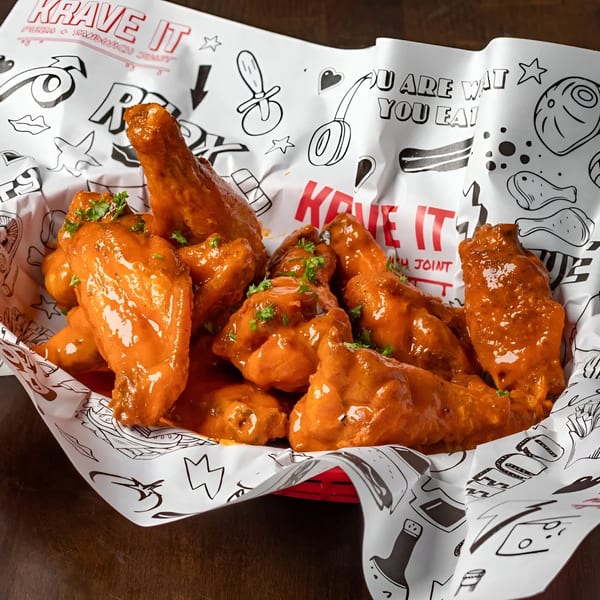 Krave It's buffalo wings, coated in orange sauce and garnished with parsley, in a branded basket.