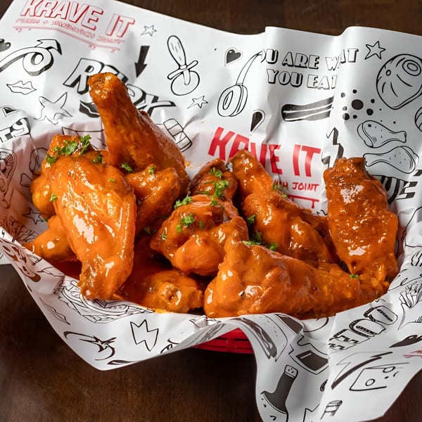 Krave It's buffalo wings, coated in orange sauce and garnished with parsley, in a red basket.